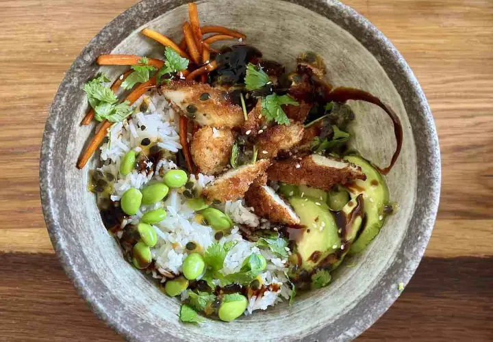 Apetyczny bowl z kurczakiem w panierce, ryżem, awokado, edamame i słodko-kwaśnym sosem.