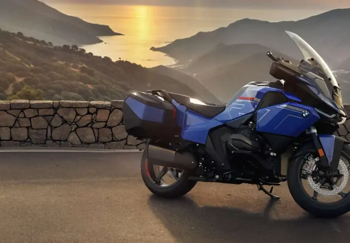 Una moto blu pronta per un viaggio avventuroso, parcheggiata su una strada panoramica con montagne e mare al tramonto.