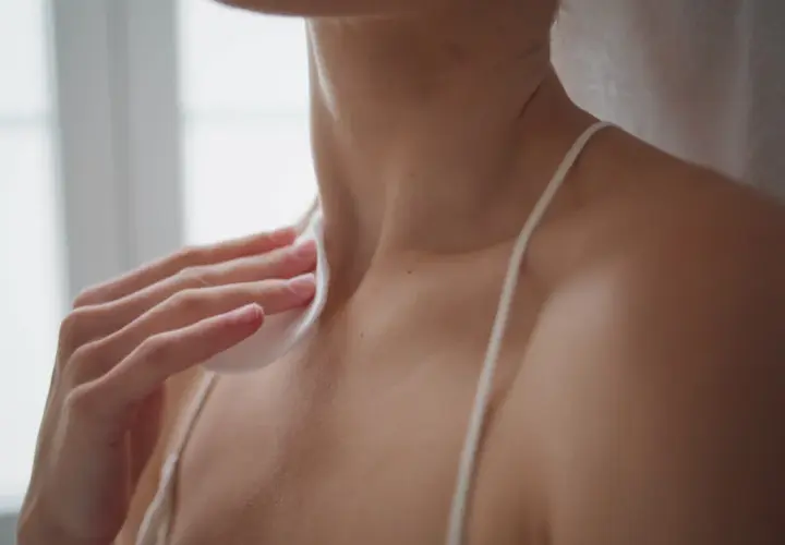 A hand holds a cotton pad to a person's neck and shoulder area.
