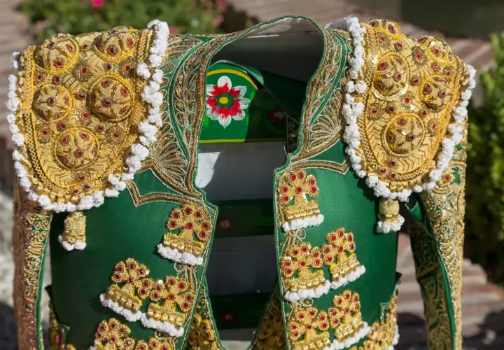 Detalle de un traje de luces de torero, con bordados dorados y pedrería roja sobre tela verde.