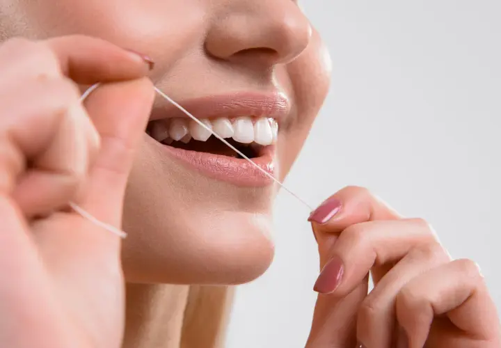 Primo piano di una donna che usa il filo interdentale per pulire i denti. Impara scovolino denti come si usa per un sorriso smagliante.