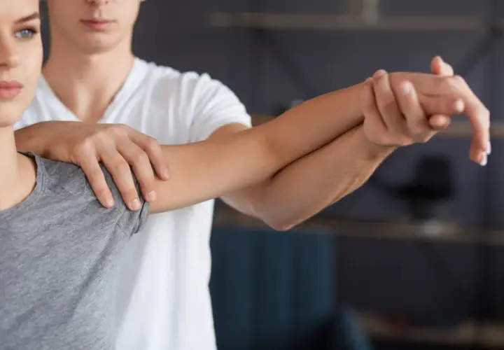 Fizjoterapeuta pomaga pacjentce z bólem łokcia golfisty, wykonując delikatne ćwiczenia rozciągające przedramię.