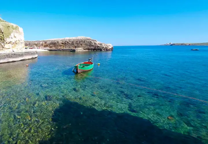 Un bateau vert et rouge flotte dans les eaux cristallines de Polignano a Mare, dans les Pouilles. Le soleil brille sur la mer Adriatique.
