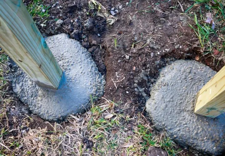 Zwei Holzpfosten werden gerade in frisch gegossenen Beton gesetzt, um sie sicher zu verankern. Das Einbetonieren von Zaunpfosten sorgt für Stabilität.