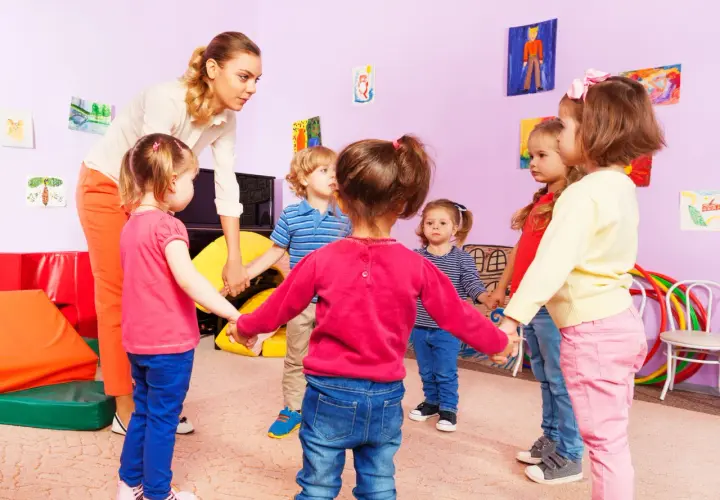 Nauczycielka z dziećmi w przedszkolu trzymają się za ręce. Czy można przenieść dziecko do innej grupy bez zgody rodziców?