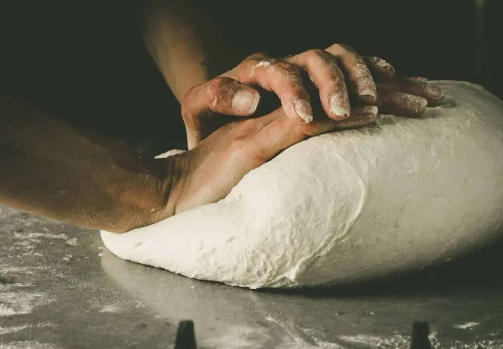 Hände kneten den Pizzateig. Die Frage "wie lange pizzateig kneten" beschäftigt jeden Bäcker.