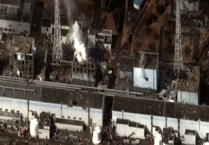 Widok z lotu ptaka na zniszczoną elektrownię Fukushima. Widać dym wydobywający się z uszkodzonych budynków, świadectwo katastrofy.
