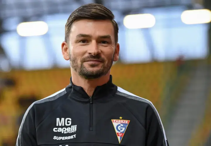 Uśmiechnięty trener Górnika Zabrze w czarnej bluzie z logo klubu.