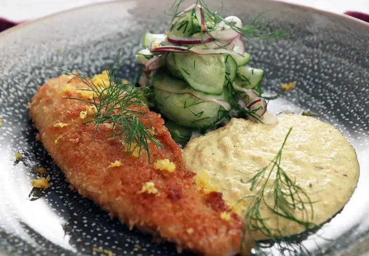 Panerad fisk med en krämig remouladsås curry, garnerad med dill och citronskal. Serveras med en fräsch gurk- och rödlökssallad.