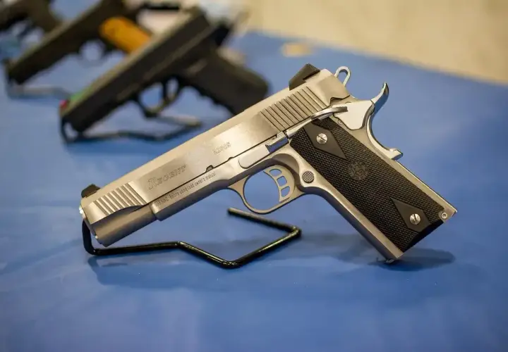 Srebrny pistolet gazowy Regent R200S na czarnym stojaku. W tle widać inne bronie.