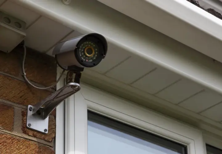 Telecamera di sicurezza, parte di un impianto di videosorveglianza, montata su una parete di mattoni sotto una grondaia.