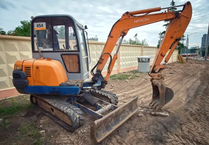 Pomarańczowa koparka Hitachi z gąsienicami i szerokim lemieszem do koparki, gotowa do pracy na budowie.