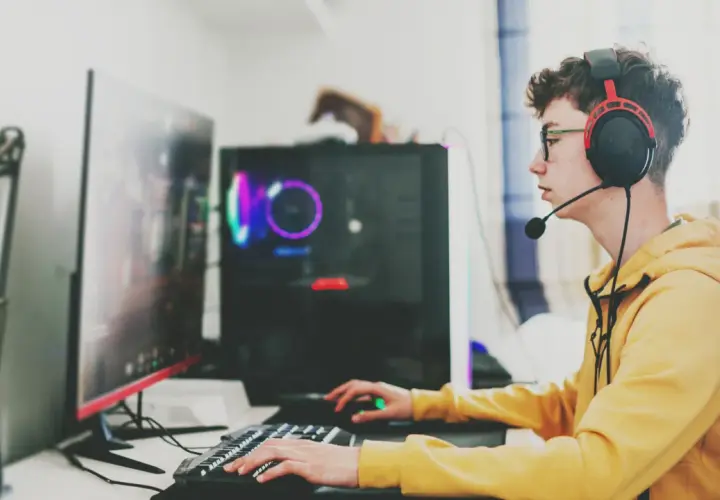 Ein junger Mann mit Kopfhörern und Brille spielt konzentriert am Computer. Sein **Computer sucht** nach neuen Herausforderungen, während er mit Tastatur und Maus agiert.