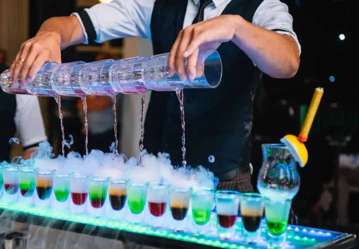 Samoobsługowy drink bar na weselu: barman nalewa kolorowe shoty z wielokomorowego shakera, tworząc efektowny pokaz.