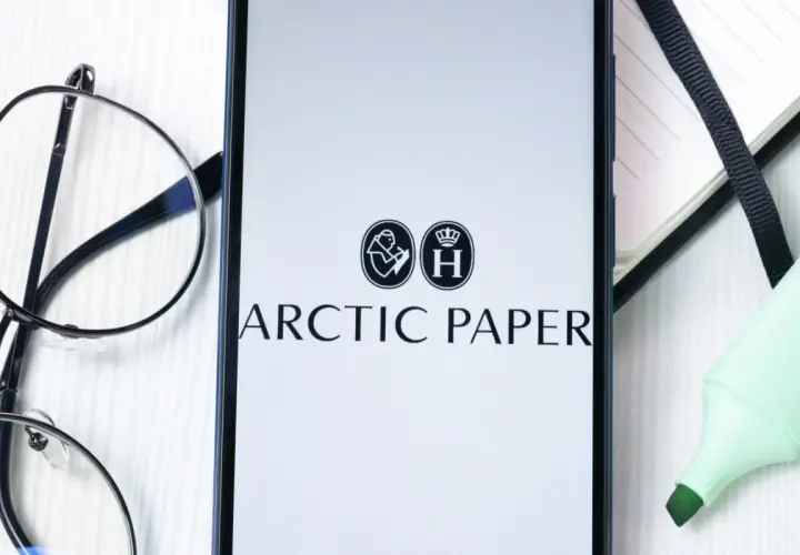 Na ekranie telefonu widnieje logo Arctic Paper. Obok leżą okulary i zielony zakreślacz, sugerując analizę akcji.