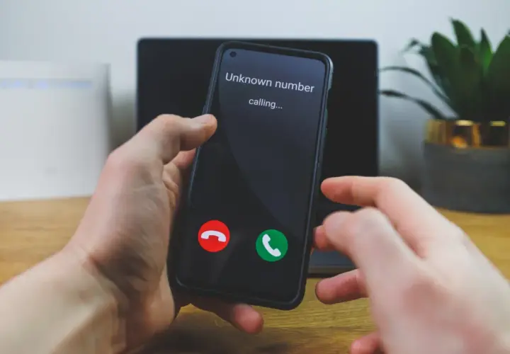 Dłoń trzyma smartfon z ekranem pokazującym "Unknown number calling..." oraz przyciski odbierania i odrzucania połączenia.