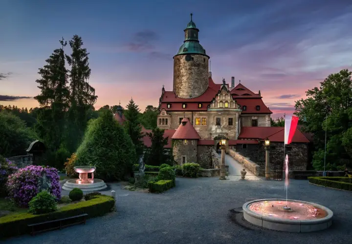 Zamek Czocha o zmierzchu, z fontannami i kwitnącymi rododendronami. Bilety do zamku można kupić online.