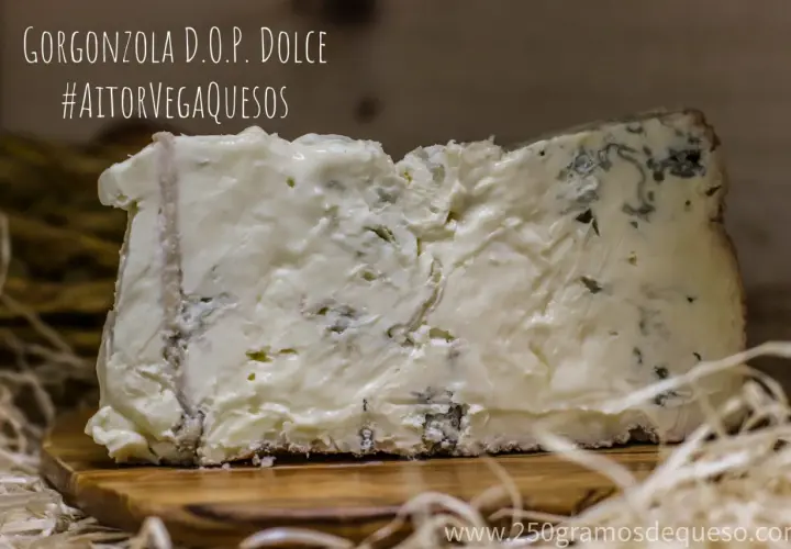 Un trozo de gorgonzola D.O.P. Dolce, un queso azul cremoso con vetas verdes y azules, sobre una tabla de madera.