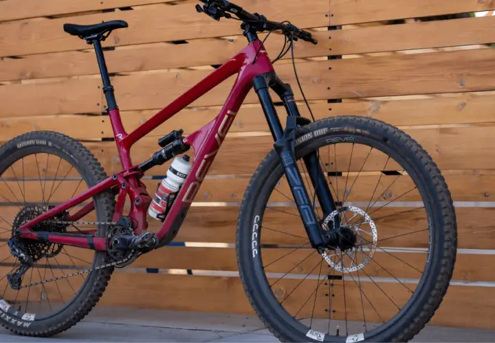 A red Revel Rail mountain bike with a water bottle, parked against a wooden fence.
