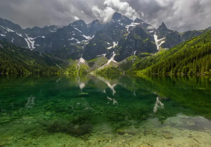 Morskie Oko z rowerem w tle, odbijające się w krystalicznie czystej wodzie. Majestatyczne góry i gęsty las tworzą malowniczy krajobraz.