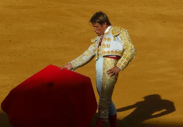Torero con traje de luces, listo para la faena de muleta, con la capa roja extendida en la arena.