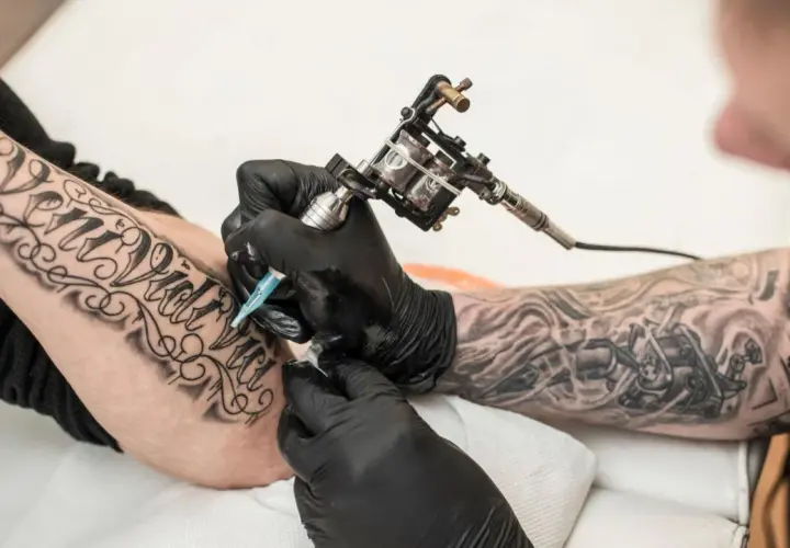 Artysta tworzy nowy tatuaż na przedramieniu klienta, używając maszynki do tatuowania.