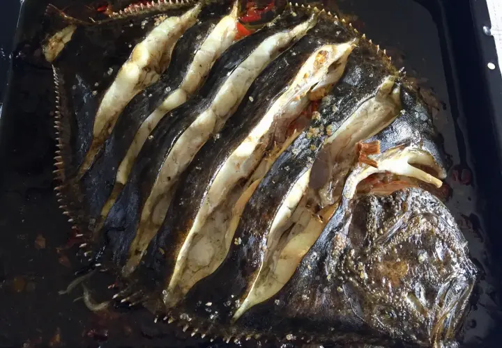Rodaballo al horno, con cortes profundos que revelan su carne blanca y jugosa, listo para ser disfrutado.