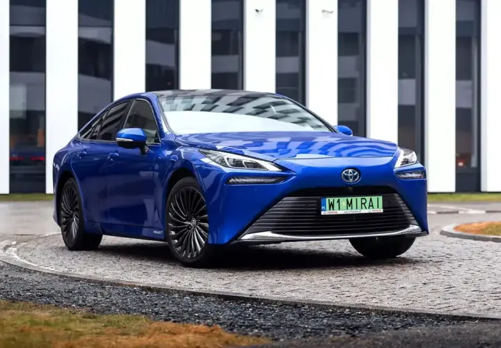 Niebieski samochód na wodór, Toyota Mirai, parkuje przed nowoczesnym budynkiem.