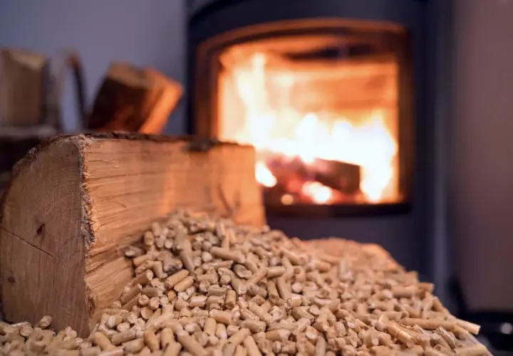 Un poêle à bois Prime Renov crache des flammes chaleureuses. Devant, une bûche et des granulés de bois attendent d'être utilisés.