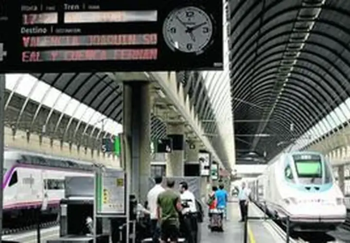 Un tren de alta velocidad espera en la estación. El panel de información muestra un destino a Valencia y Sevilla.