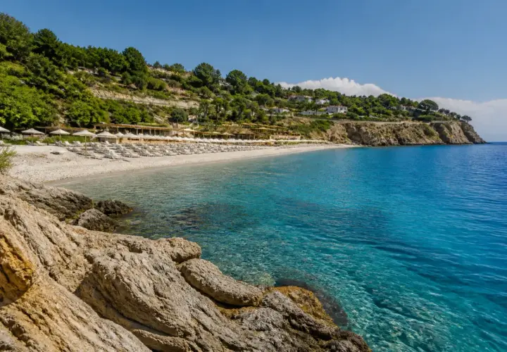 Plage de galets et eaux turquoises à Alassio, Italie. Des rangées de parasols et de chaises longues invitent à la détente sous le soleil.
