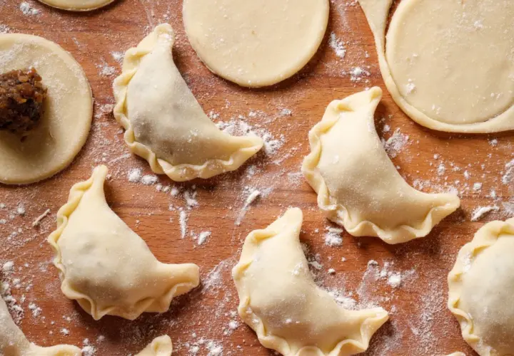 Surowe pierogi z kaszą gryczaną i twarogiem na drewnianej desce, posypane mąką.