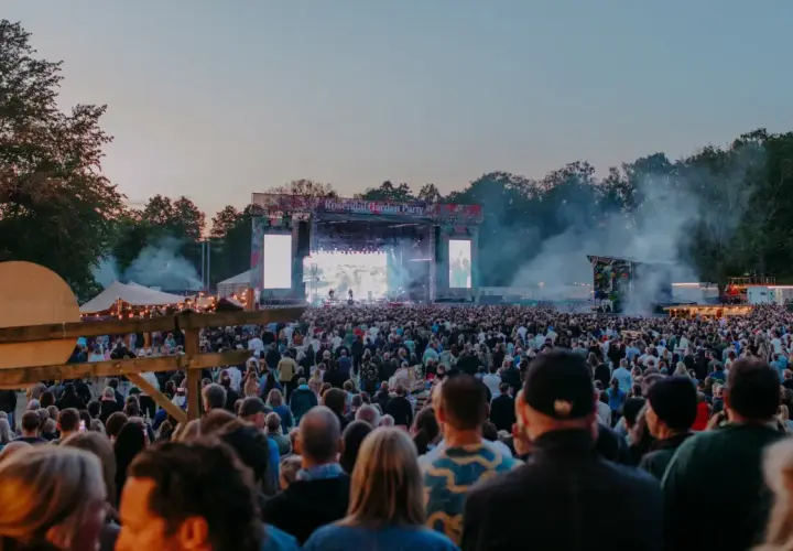 Stor publik vid Rosendal Garden Party. En stor scen med artister och ljusspel, omgiven av träd och tält.