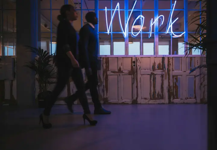 Ludzie idą w stronę neonu "Work", symbolizującego misję i wizję firmy.