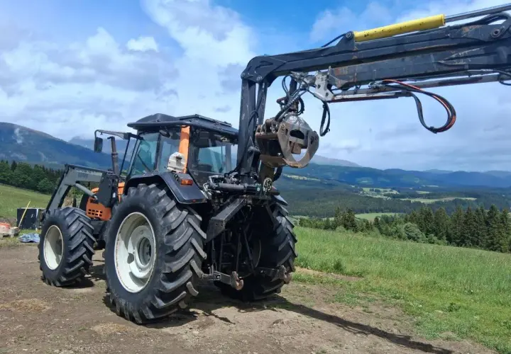 Ein gebrauchter Forstkran mit Greifer an einem Traktor, bereit für den Einsatz im Wald.