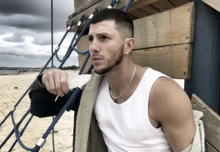 Sasha top model, z piórkiem w dłoni, na tle plaży i chmur.