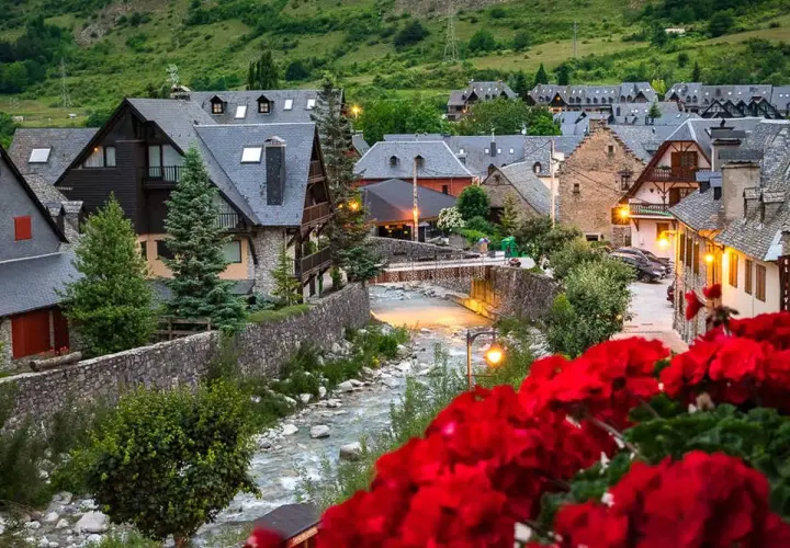 Pueblo pintoresco en el Pirineo Catalán, con casas de piedra y tejados grises junto a un río. Flores rojas en primer plano.