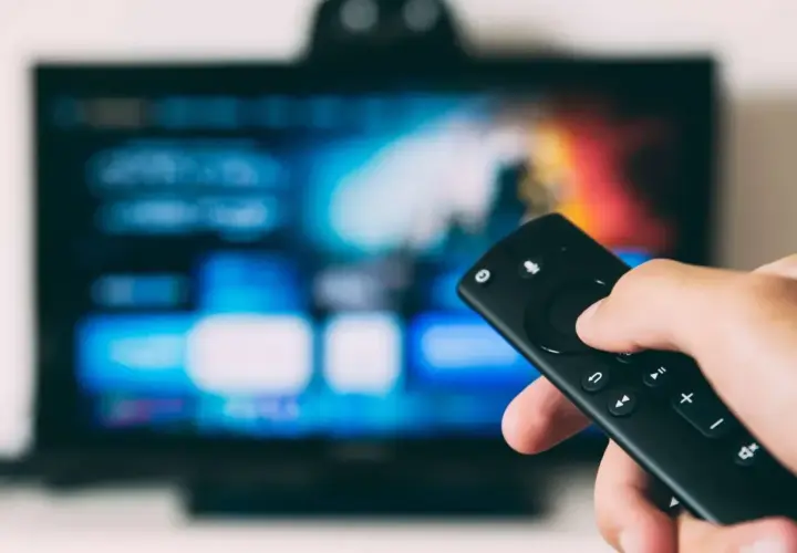 Dłoń trzymająca pilot do telewizora, ekran pokazuje menu. Dowiedz się, jak odbierać TV naziemną bez anteny, korzystając z nowoczesnych rozwiązań.