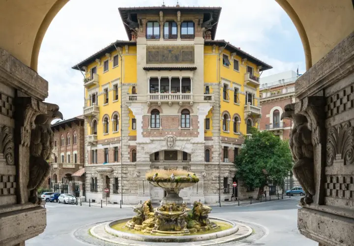 Fontana e palazzo giallo in stile Coppedè, con dettagli scultorei e un'atmosfera d'altri tempi.