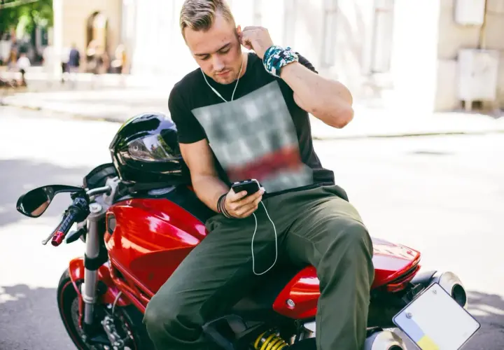 Joven en moto roja ajusta sus auriculares. Disfruta de su música, demostrando que es legal escuchar música en moto.