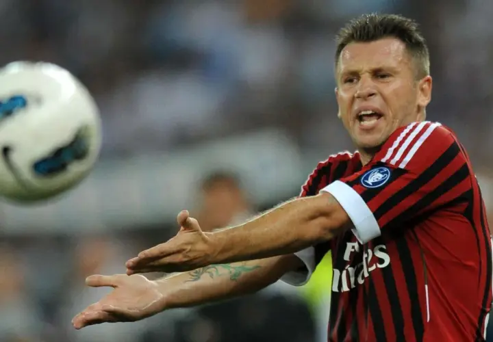 Piłkarz Cassano w koszulce Milanu, z wyrazem frustracji na twarzy, gestykuluje w stronę lecącej piłki.