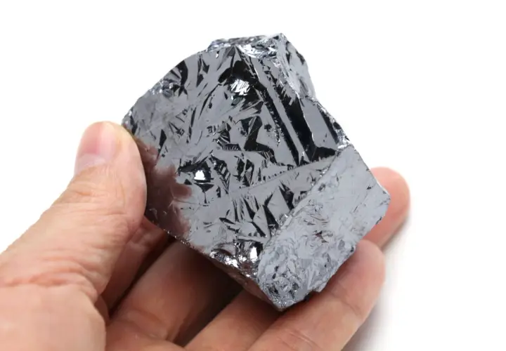 Ein Mensch hält ein Stück Silizium, dessen Oberfläche wie eine glänzende, metallische Haut mit komplexen Mustern aussieht.