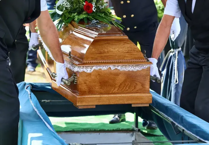 Pogrzebowa drewniana trumna z kwiatami, niesiona przez ludzi w białych rękawiczkach. Kto nie dostanie zasiłku pogrzebowego?