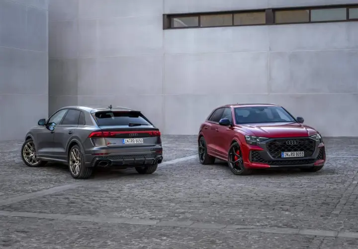 Due Audi RS Q8, una grigia e una rossa, parcheggiate su un selciato di fronte a un edificio moderno.