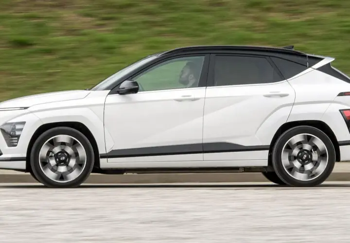 Biały Hyundai Kona w ruchu, z czarnym dachem i przyciemnianymi szybami. Kierowca widoczny w kabinie. Sprawdź hyundai kona wymiary.