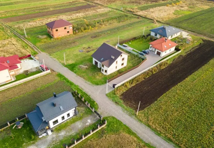 Widok z lotu ptaka na kilka domów jednorodzinnych na tle pól i zieleni.