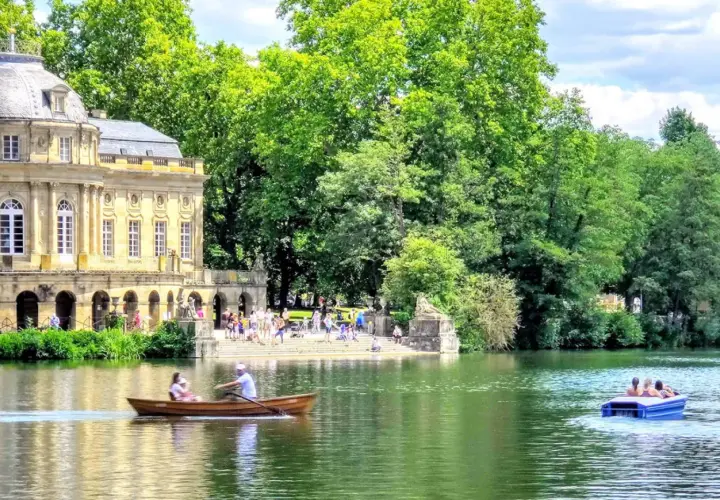Ein sonniger Tag am Monrepos Schloss. Menschen genießen Bootsfahrten auf dem See vor dem barocken Gebäude, umgeben von üppigem Grün.