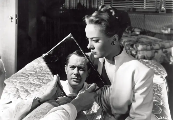 Kobieta trzyma lustro, w którym odbija się mężczyzna z blizną na twarzy. Klimat typowy dla **film noir**.