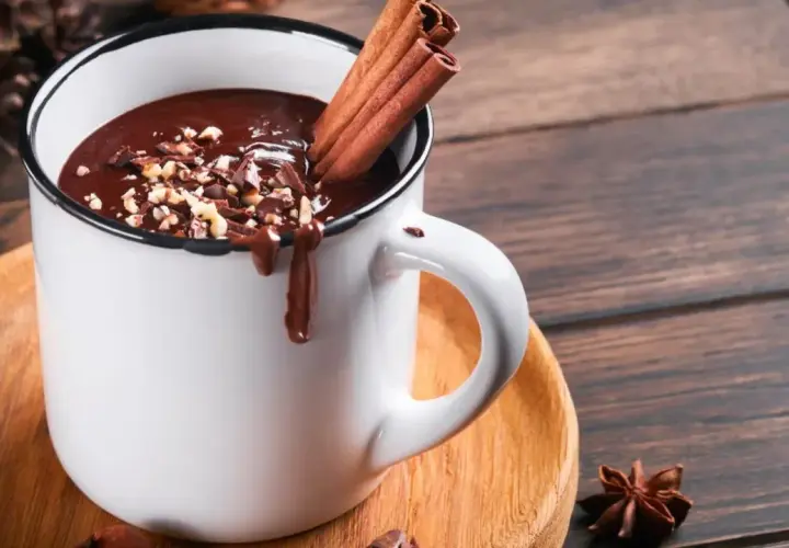 Un déliceux chocolat chaud crémeux, garni de noisettes concassées et de bâtons de cannelle, prêt à réchauffer vos journées.