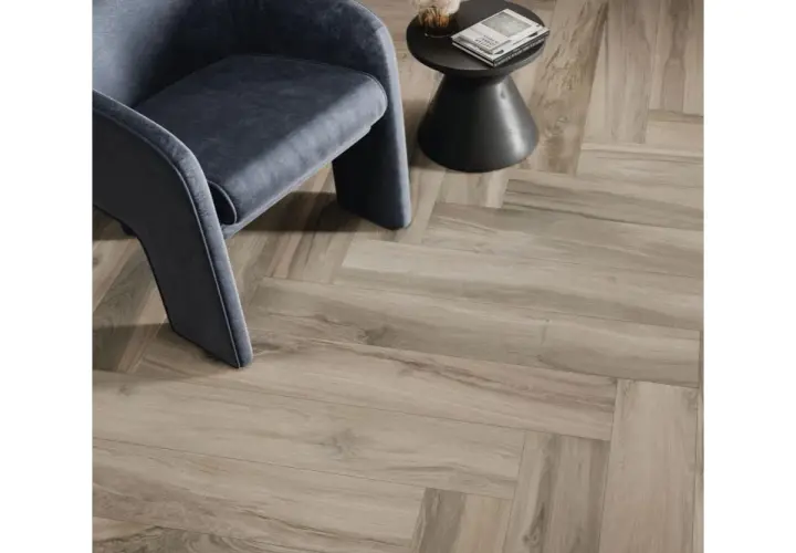 Un fauteuil moderne repose sur un sol en pose carrelage imitation parquet en chevrons, créant une ambiance chaleureuse et élégante.